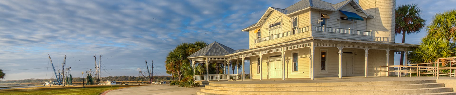Seaside house with porch and palm trees under a partly cloudy sky.