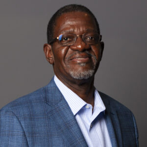 Portrait of a man in a blue suit and glasses, smiling against a gray background.