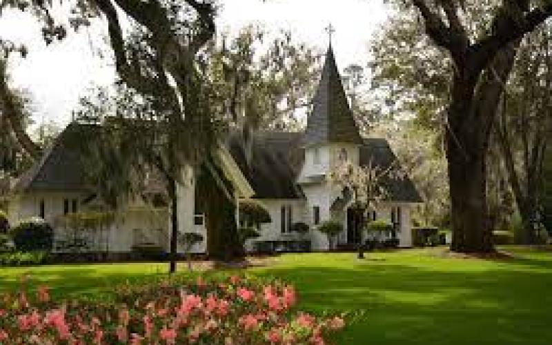Charming church with steeple, surrounded by trees and a lush green lawn.