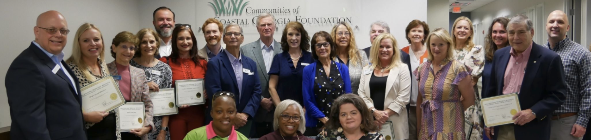 Group of award recipients smiling, holding certificates indoors.