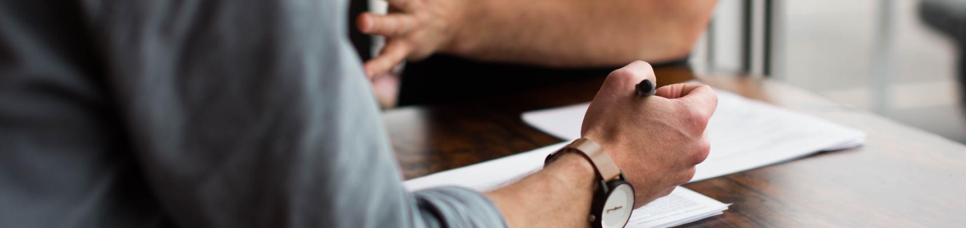 Two people discussing papers at a wooden table.